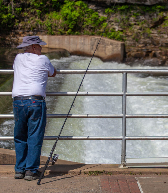 Fisherman along the Redbank Creek standing next to his fishing pole at the dam in New Bethlehem, PA on a sunny day