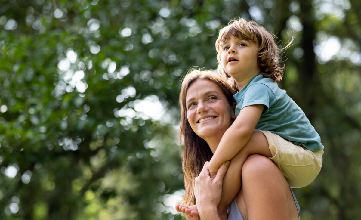 Happy mother carrying her son on her shoulders at the park and smiling - family lifestyle concepts