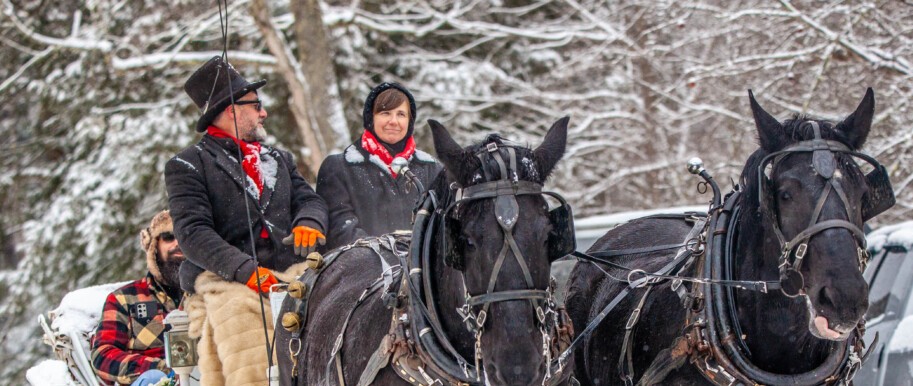 Two people riding in a horse and carriage in the snow at Snowman in the Forest in Cook Forest State Park